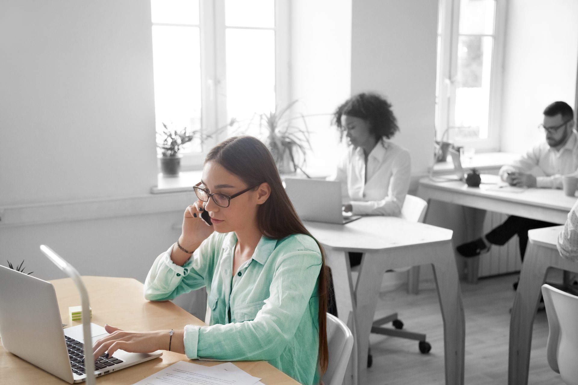 Woman wearing glasses sitting at desk while on the phone