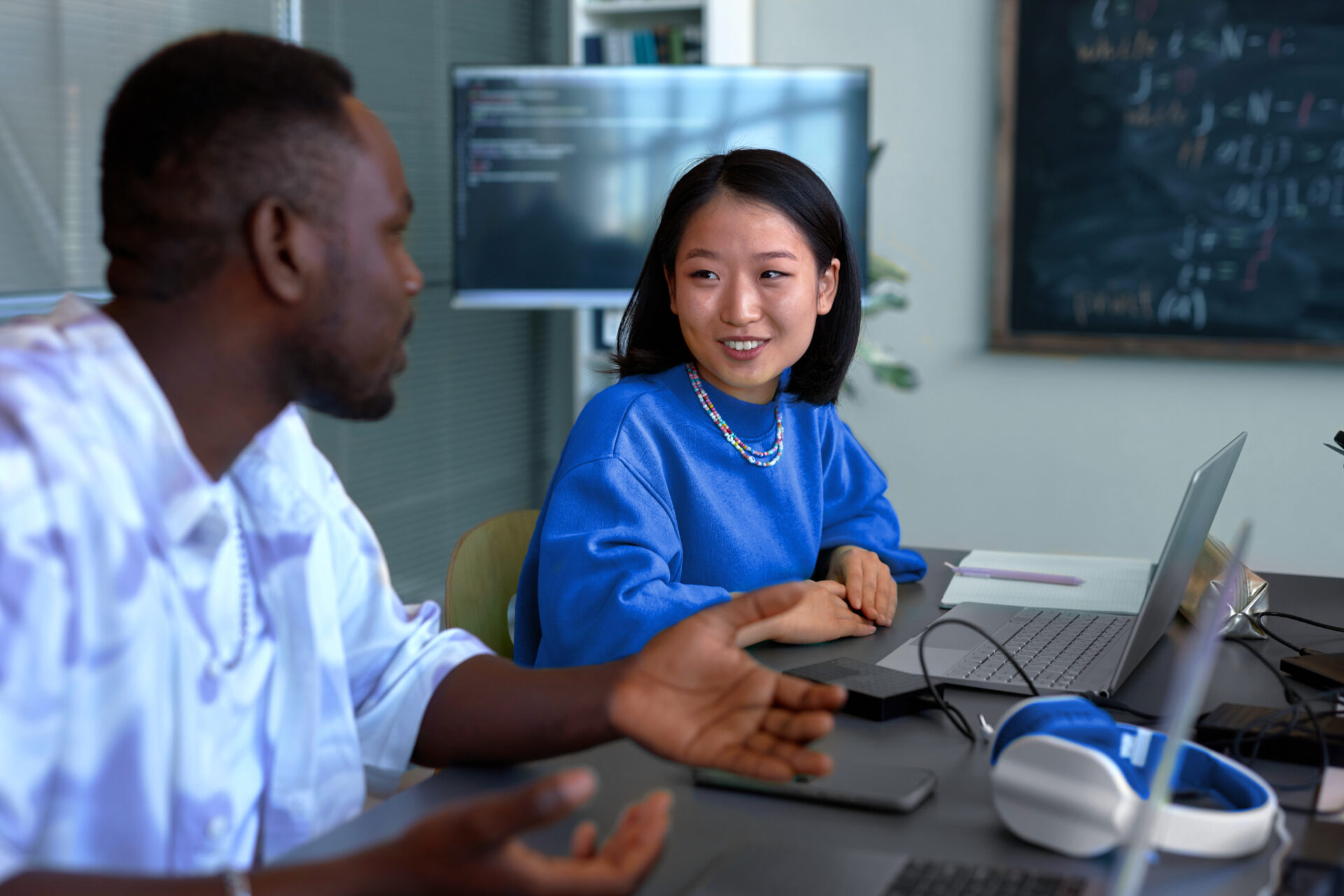 A man and woman collaborate in an office setting with laptops and a VR headset on the table, discussing AI-driven solutions for streamlining the financial close process.