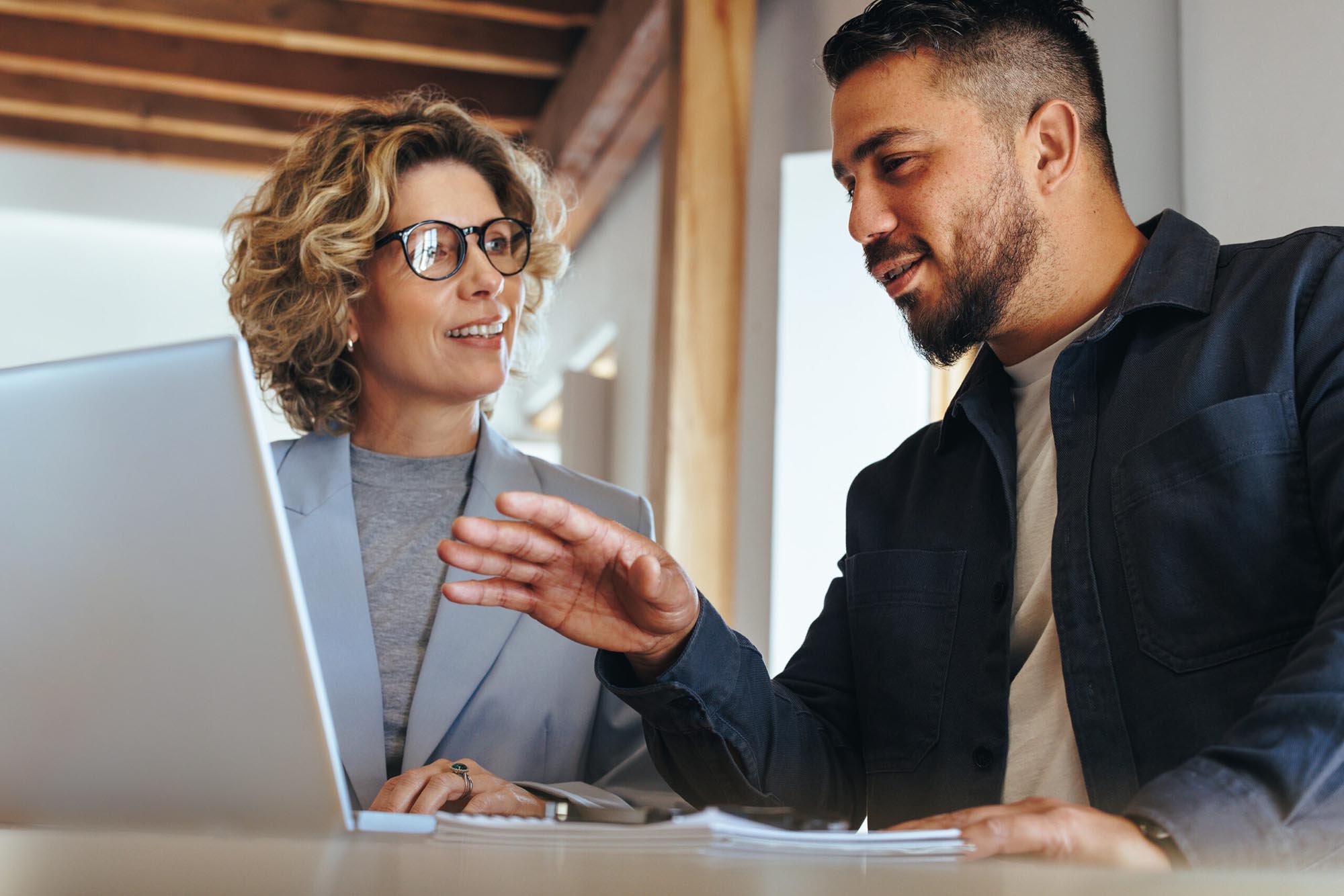 Two professionals discussing financial close management tasks while reviewing laptop in office